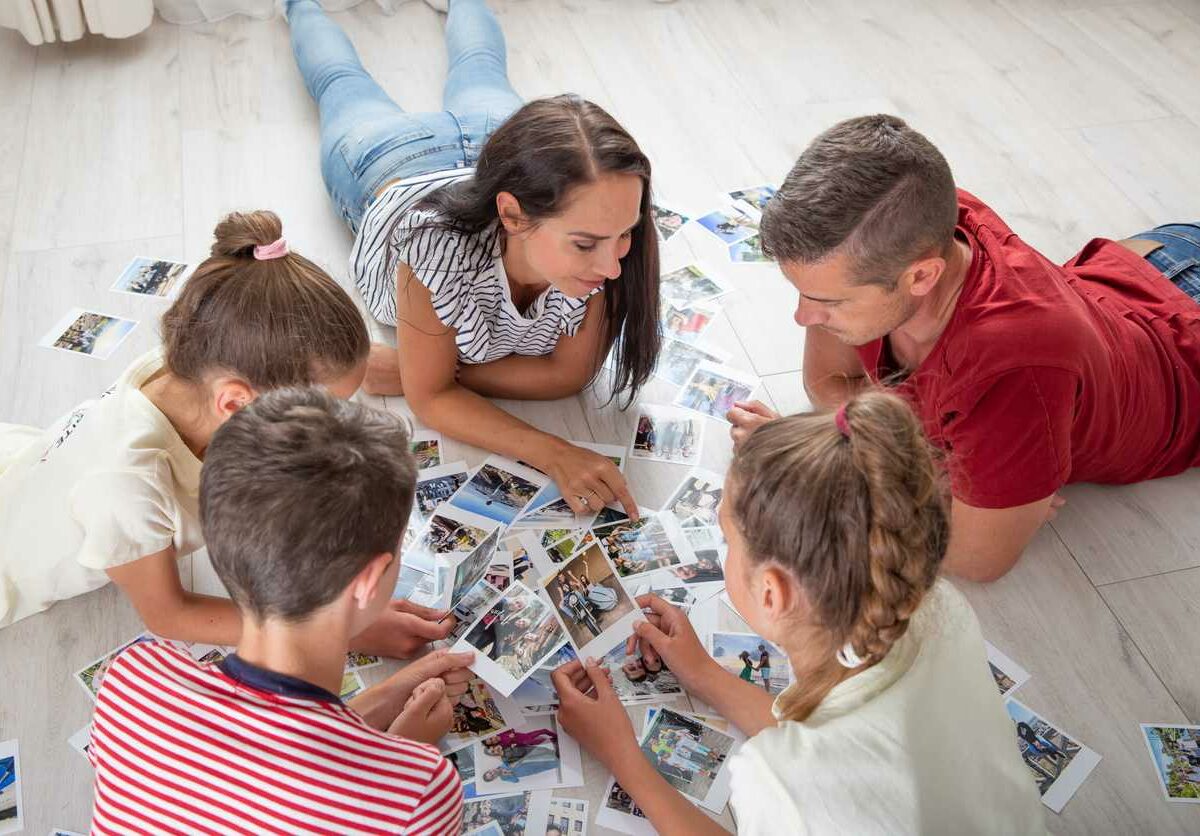 A family of parents and three children lay on a floor around a spread of photos looking at and pointing to them.