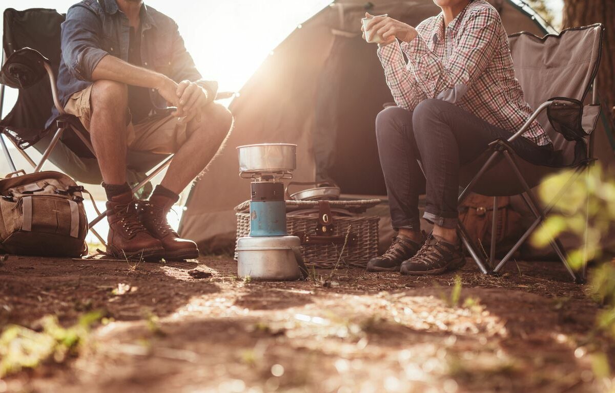 A couple cooks a meal while sitting outside their tent on the campground.