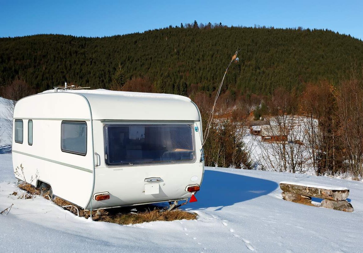 RV camped on a snow-covered field by the mountains on a sunny day.