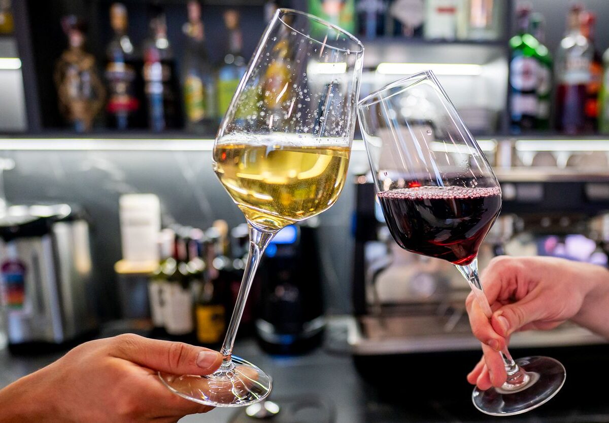 Two people toasting and clinging glasses of wine inside a winery.