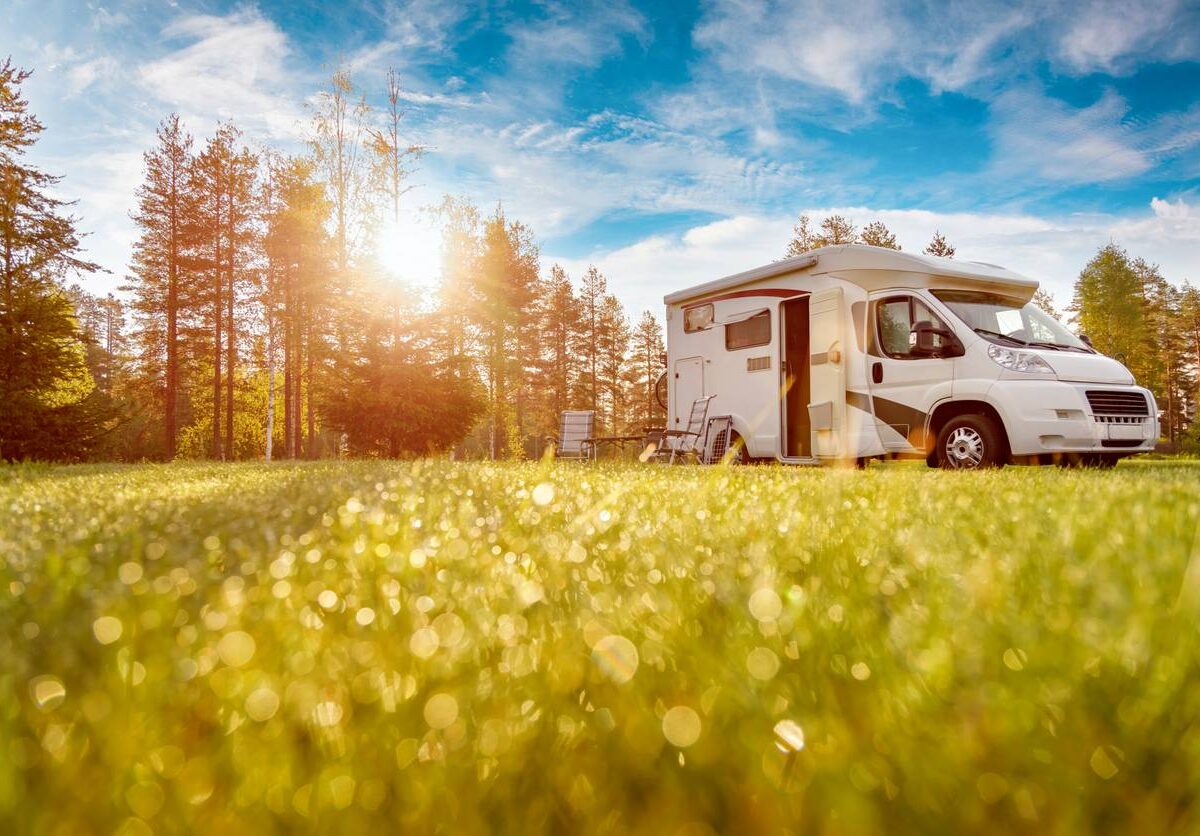 An RV is camped in a field next to a forest as its drivers enjoy a great camping trip.