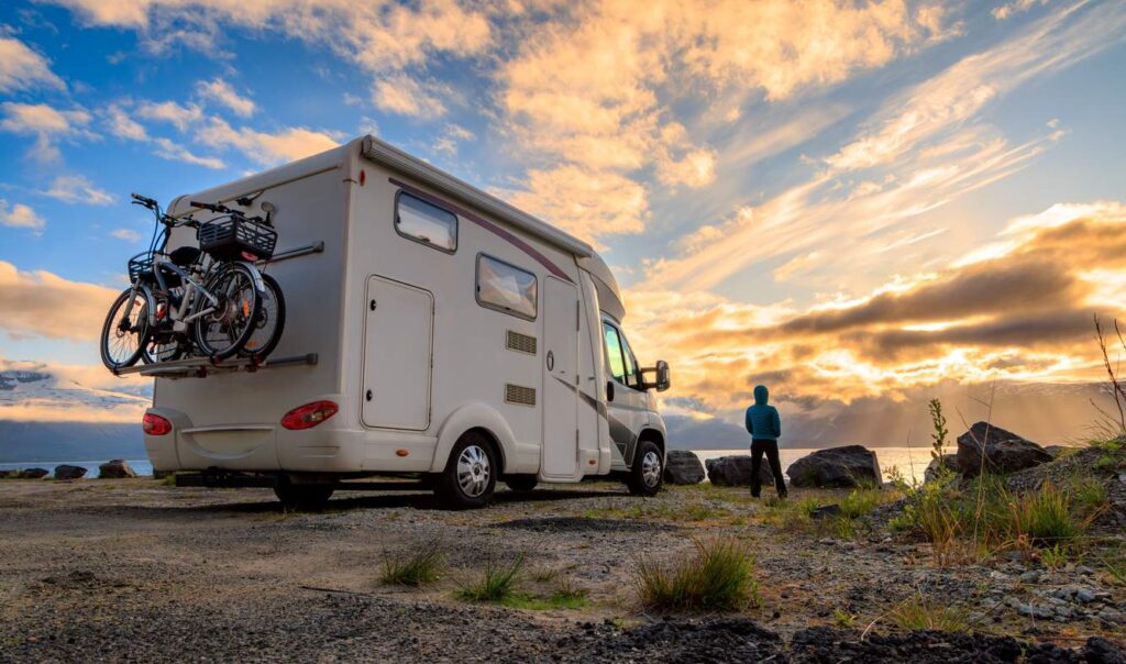 A child in a jacket stands to view the sunset next to their family’s RV.